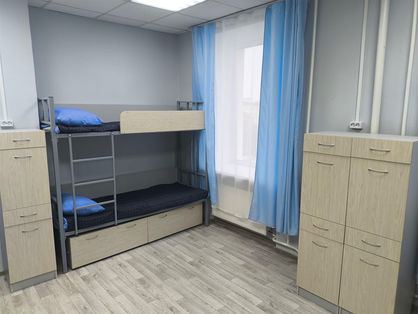 Комната в хостеле: двухъярусная кровать, шкафы, окно с голубыми шторами